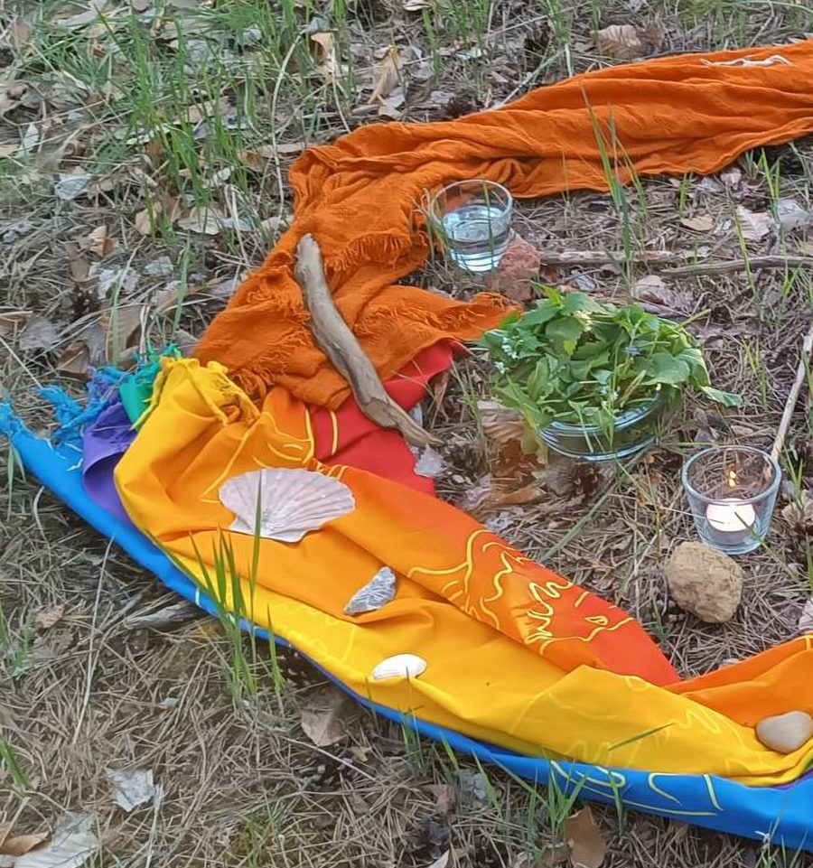 Eine Ritualmitte auf dem Waldboden aus bunten Tüchern, Muscheln, Steinen, Kräutern und Kerzen